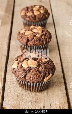 Image verticale de trois muffins au chocolat alignés sur un fond en bois. Banque D'Images