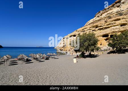 Matala, Grèce - 07 octobre 2018 : personnes non identifiées sur la plage de sable avec des tombes anciennes sur la droite et des îles de Paxidadia sur fond Banque D'Images