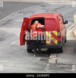 Un postman collecte ses livraisons à l'arrière de sa camionnette avant sa livraison finale de la journée. Banque D'Images