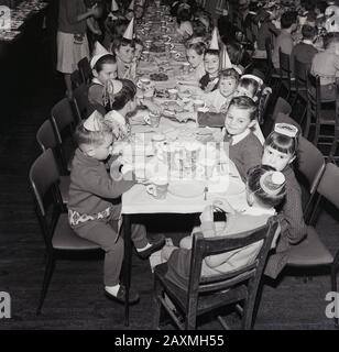 Années 1960, historique, dans une salle à manger, de jeunes écoliers dans des chapeaux de fête s'amusant ensemble à un repas de noël, Angleterre, Royaume-Uni Banque D'Images