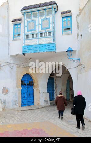 Rue typique pavée et étroite à l'intérieur de la médina historique de Kairouan en Tunisie, avec des couleurs bleues et blanches, des arcades et un balcon traditionnel Banque D'Images