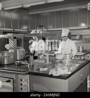 Années 1960, historique, deux chefs masculins portant des uniformes traditionnels ou des chapeaux blancs et hauts du chef - travaillant dans une grande cuisine, Angleterre, Royaume-Uni. Banque D'Images