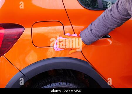 L'homme après le nettoyage nettoie sa voiture orange avec un chiffon rose au lavage de voiture. Fermeture de la main et du corps de la voiture. Banque D'Images