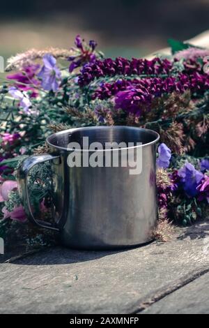 Mug en métal sur une table avec des fleurs qui y sont couchées Banque D'Images