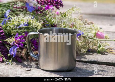 La tasse en métal touristique à côté des fleurs se dresse sur une table en bois gris Banque D'Images