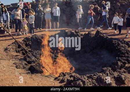 Lanzarote, îles Canaries, Espagne - 28 déc. 2019: Le volcan Timanfaya chauffe-sol provoquant un feu brûlant de balle de foin dans le parc national de Timanfaya à Lanzarote. Les touristes regardent le feu. Banque D'Images