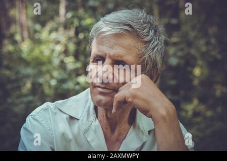 un vieil homme pensant à la toile de fond de verdure, filtre sombre Banque D'Images