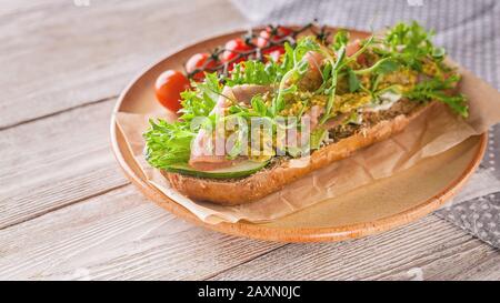 Bannière alimentaire : bruschetta avec viande fumée brute, fromage à la crème, sauce aux petits pois et au pesto, tomates cerises sur une plaque en céramique ronde Banque D'Images