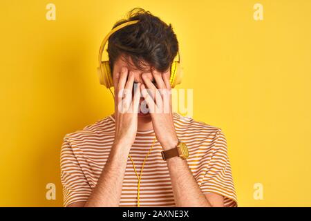 Adolescent portant un casque sur fond jaune isolé souffrant de maux de tête désespérés et stressés parce que la douleur et la migraine. Mains sur la hea Banque D'Images