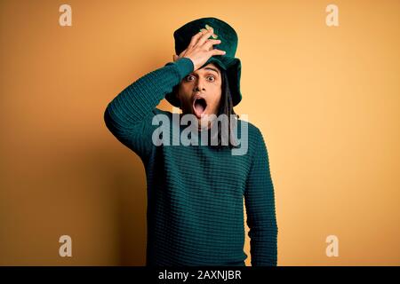 Jeune homme africain américain portant un chapeau vert avec un trèfle célébrant saint patricks jour surpris avec la main sur la tête pour erreur, se souvenir de l'erreur. Va-Et-Car Banque D'Images