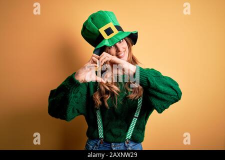 Belle femme brunette portant un chapeau vert avec un trèfle célébrant saint patricks jour souriant dans l'amour montrant le symbole du coeur et la forme avec les mains. Romain Banque D'Images