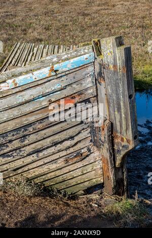 une ancienne épave ou coque d'un vieux bateau en bois toronné sur le rivage et pourriture sur les méplats de boue et la haute marque côtière de marée. Banque D'Images