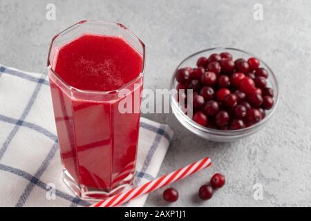 Un verre avec jus de canneberges maison et un bol de canneberges sur une table en béton gris Banque D'Images