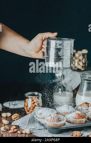 Tamisez le sucre en poudre sur un délicieux cupcake avec des raisins secs, des amandes et des noix dans la cuisine. Une femme âgée tamisait le sucre en poudre par tamis sur la vanille c Banque D'Images