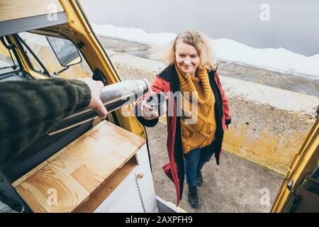 Jeune blonde se tenant à côté de la camionnette qui surplombe la mer d'hiver gelée. Vue par la porte ouverte. Banque D'Images