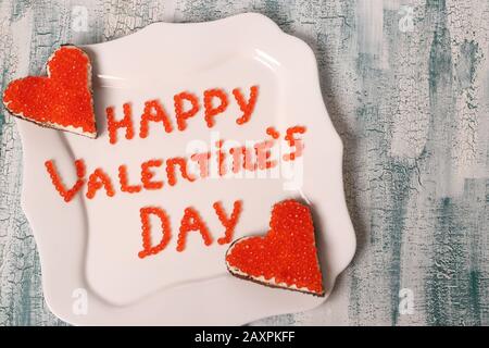 L'inscription Bonne Saint Valentin de caviar rouge sur une plaque blanche avec des canapés, vue sur le dessus Banque D'Images