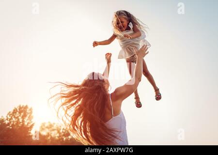 Fête des mères. Femme jouant et s'amuser avec sa fille dans le parc d'été. Mère qui lance sa fille à l'extérieur. Banque D'Images