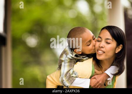 Le jeune garçon afro-américain embrasse sa mère sur la joue alors qu'elle lui donne un dos piquante. Banque D'Images