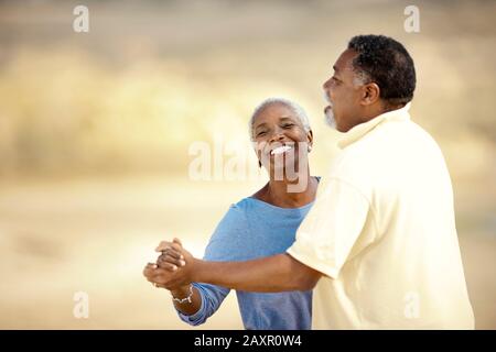 Couple senior souriant dansant sur une plage. Banque D'Images