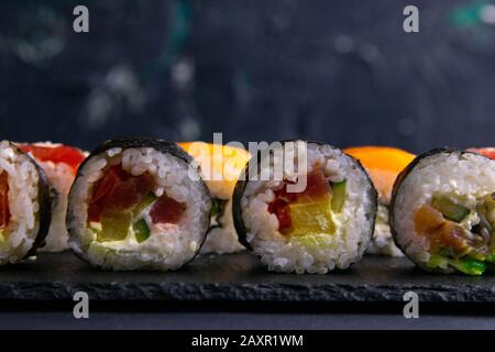 Différents types de rouleaux se tiennent sur un plateau en granit noir pour les sushis sur fond noir Banque D'Images