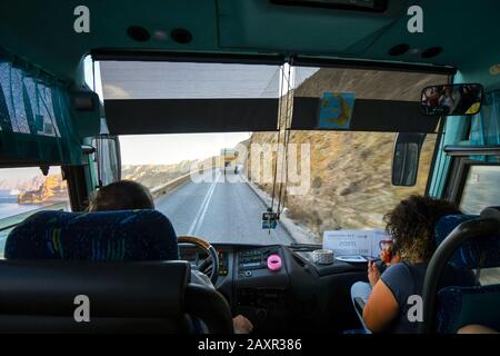 La vue de l'intérieur d'un bus de visite le long de la route sinueuse de colline d'Oia au port de Santorin Grèce, avec la mer et bateau de croisière au loin Banque D'Images
