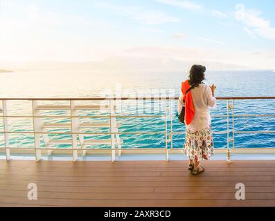 Une jeune femme brunette aime prendre un verre sur le pont extérieur d'un bateau de croisière dans la mer Méditerranée au lever du soleil. Banque D'Images
