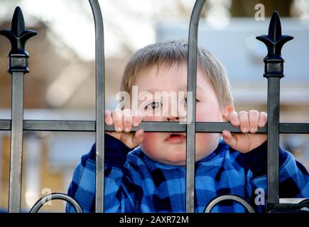 Très petit enfant regardant par une porte en métal, le gardant en sécurité Banque D'Images