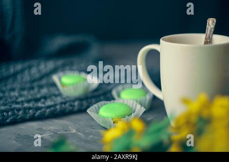 Café chaud avec lait ou crème et macarons verts sur la table de loft dans un cadre romantique avec chrysanthèmes à proximité Banque D'Images