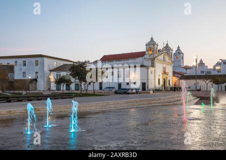 Place de la République avec fontaines lumineuses et église Sainte-Marie Igreja de Santa Maria, Lagos, Algarve, district de Faro, Portugal Banque D'Images