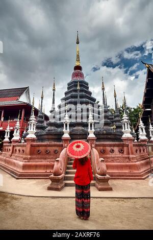 Femme avec parapluie thaïlandais traditionnel rouge qui regarde le temple noir Wat Phan Tao à Chiang Mai, Thaïlande Banque D'Images