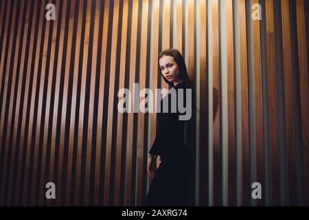 Une jeune fille passe devant un mur en bois et regarde dans l'appareil photo. Portrait d'une belle fille à poil long à l'arrière-plan un mur en bois Banque D'Images