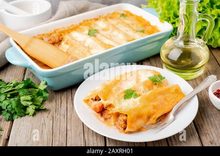 Cannelloni avec remplissage de bœuf haché, tomates, cuites avec sauce tomate bechamel, vue latérale, vieux fond en bois sombre Banque D'Images