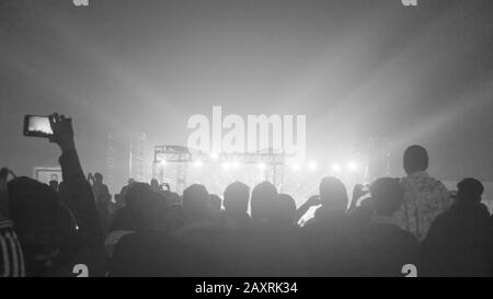 Silhouette d'un grand public foule de personnes heureuses se tenant dans les terrains de concert applaudissant le clapping utiliser des smartphones se levant les mains dans l'air face à la musique b Banque D'Images