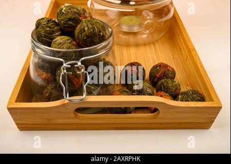 Boulettes de thé aux fleurs dans un pot en verre et thé aux fleurs brassées dans une théière en verre sur un plateau en bois sur fond blanc. Gros plan Banque D'Images