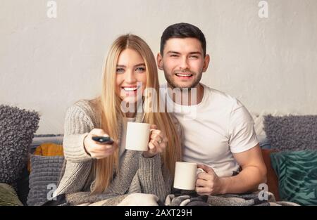 Un couple joyeux millénaires qui boit du thé et regarde la télévision Banque D'Images