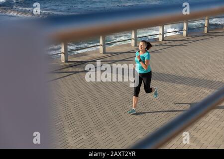 Vue latérale à angle élevé d'une femme caucasienne d'âge moyen mûre qui travaille sur une promenade le jour ensoleillé, en course à pied Banque D'Images