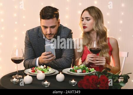 Femme Jalouse Randonnée Dans Le Smartphone De Boyfriend Pendant Le Dîner Au Restaurant Banque D'Images