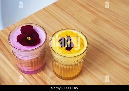 Latte coloré fantaisie avec mousse de lait rose et jaune dans des tasses en verre Banque D'Images