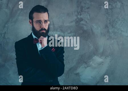 Portrait de son beau homme sombre triste sulen barbu gars portant tux pensant décider isolé sur fond de mur industriel gris de béton Banque D'Images