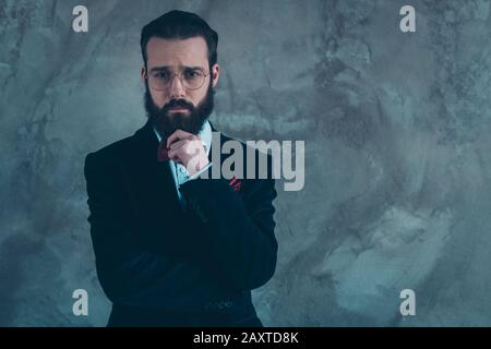 Portrait de son sympathique sympathique homme bien habillé triste barbu portant tuxedo pensant isolé sur le fond de mur industriel gris de béton Banque D'Images