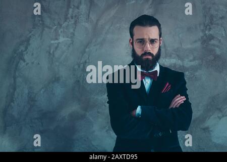 Portrait de son sympathique sympathique gars à barbe puzzled sullen portant des bras repliés tux isolés sur fond de mur industriel gris en béton Banque D'Images