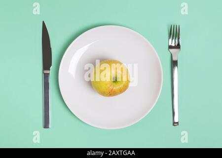 Pomme verte entière sur une plaque blanche avec fourche et couteau allongé près, vue de dessus. Banque D'Images