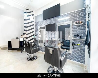 Salon de beauté moderne et lumineux. Salon de coiffure intérieur d'affaires avec un look industriel minimaliste. Décoration noire et blanche avec miroirs, chaises, écran de télévision et m Banque D'Images