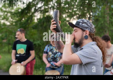 Krasnoyarsk, Russie, 30 juin 2019: Un homme est un jeune homme soufflant une corne, autour des hommes jouant des tambours. Un groupe musical se produit en été dans une op Banque D'Images