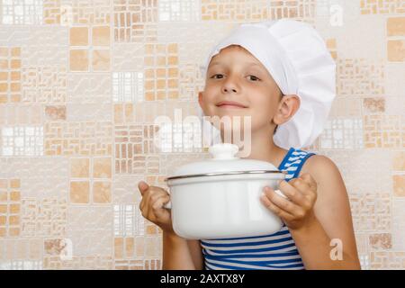 Un garçon souriant dans la bonne adresse d'un cuisinier avec une poêle dans ses mains Banque D'Images