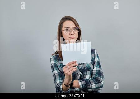 une femme insultée avec des lunettes montre une feuille de papier blanche Banque D'Images