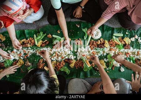 Top View portrait des gens asiatiques manger leur nourriture servie sur le dessus de la feuille de banane se poser sur le sol. Kembulan javanais tradition de manger Banque D'Images