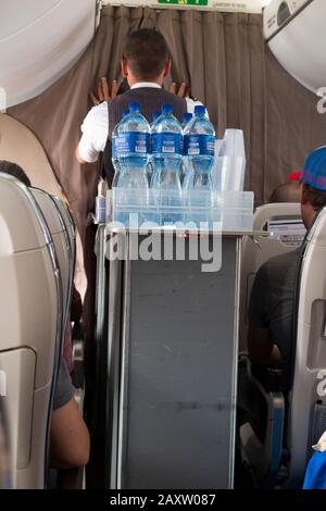 Un membre de l'équipage de cabine avec un chariot pour boissons nautiques regarde à travers les rideaux/le rideau entre les passagers Economy et les sièges en classe affaires sur un avion d'avion d'avion d'avion d'avion d'avion de Bombardier. (112) Banque D'Images