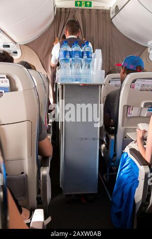 Un membre de l'équipage de cabine avec un chariot pour boissons nautiques regarde à travers les rideaux/le rideau entre les passagers Economy et les sièges en classe affaires sur un avion d'avion d'avion d'avion d'avion d'avion de Bombardier. (112) Banque D'Images