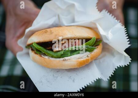 Cuisine de rue. Hamburger avec épinards, fraises et canard. Les mains des hommes tiennent un hamburger Banque D'Images